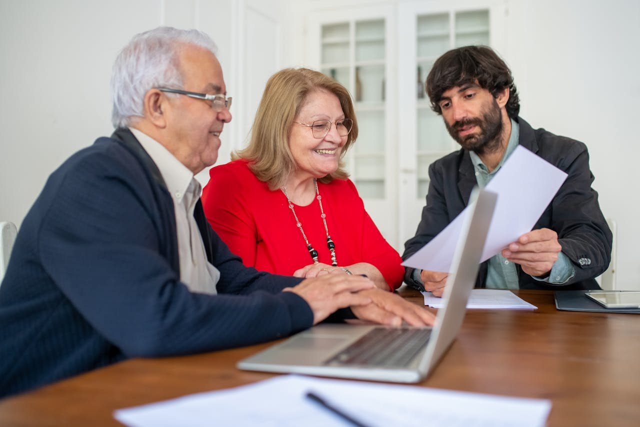 A financial advisor discusses paperwork with a client at a desk in a modern office.